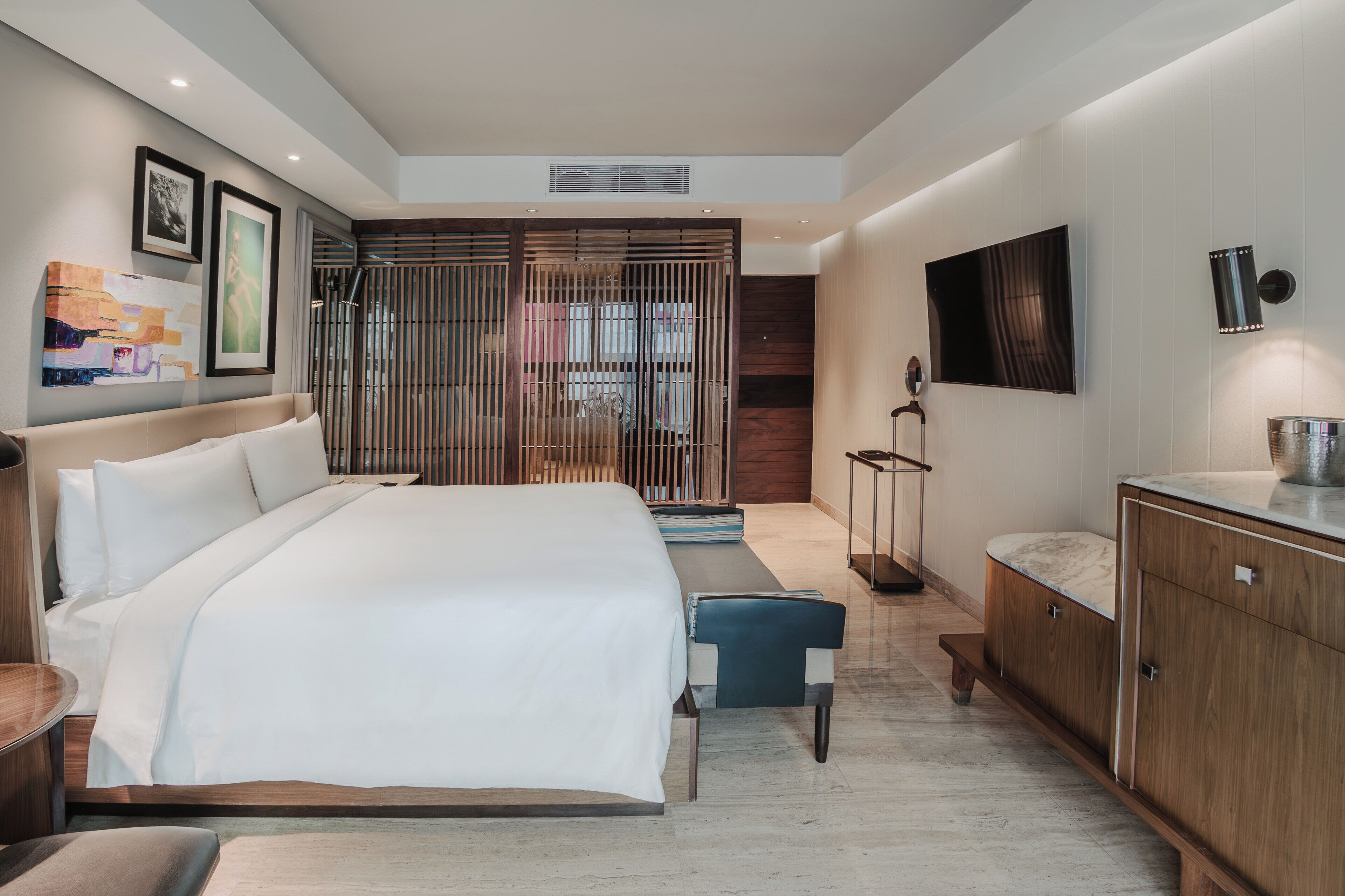 Una habitación de hotel moderna con una cama grande, un escritorio, un televisor y obras de arte en las paredes.