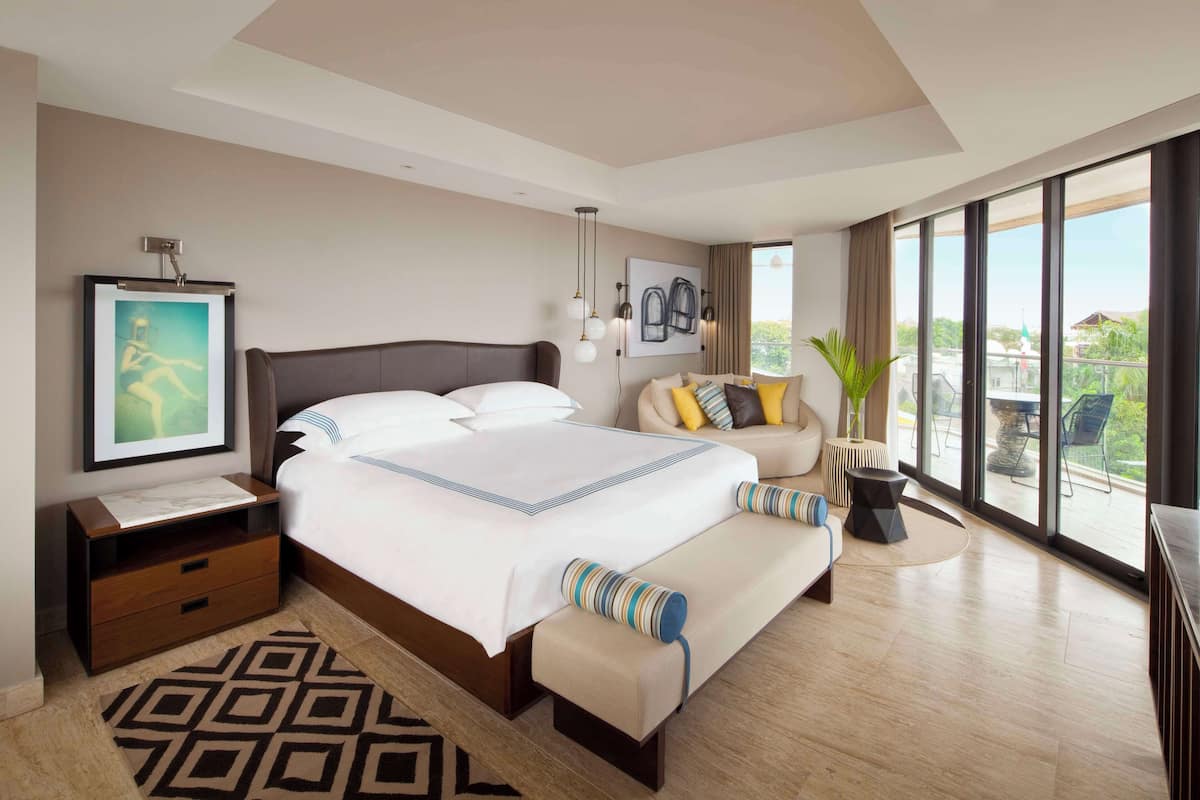 Quarto de hotel moderno com uma cama grande, um sofá, um espaço de refeições e uma varanda com vista.