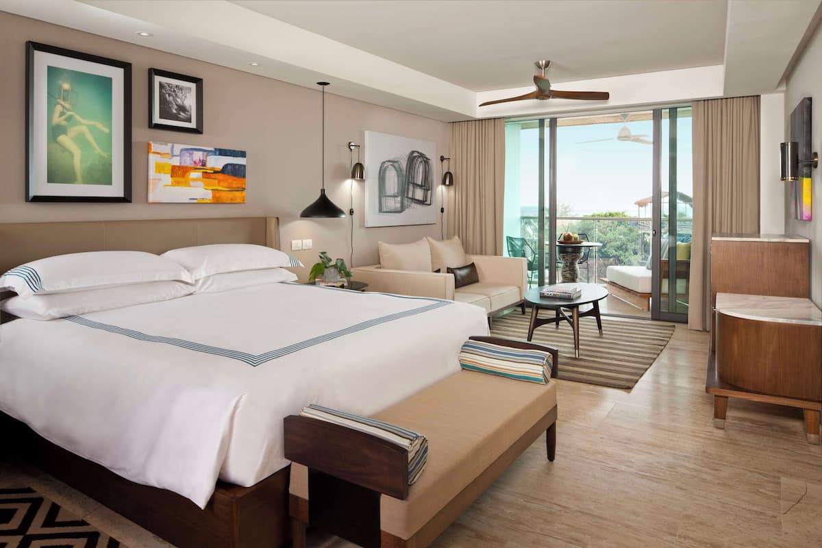 Quarto de hotel com uma cama grande, um sofá, uma mesinha e varanda com vista.