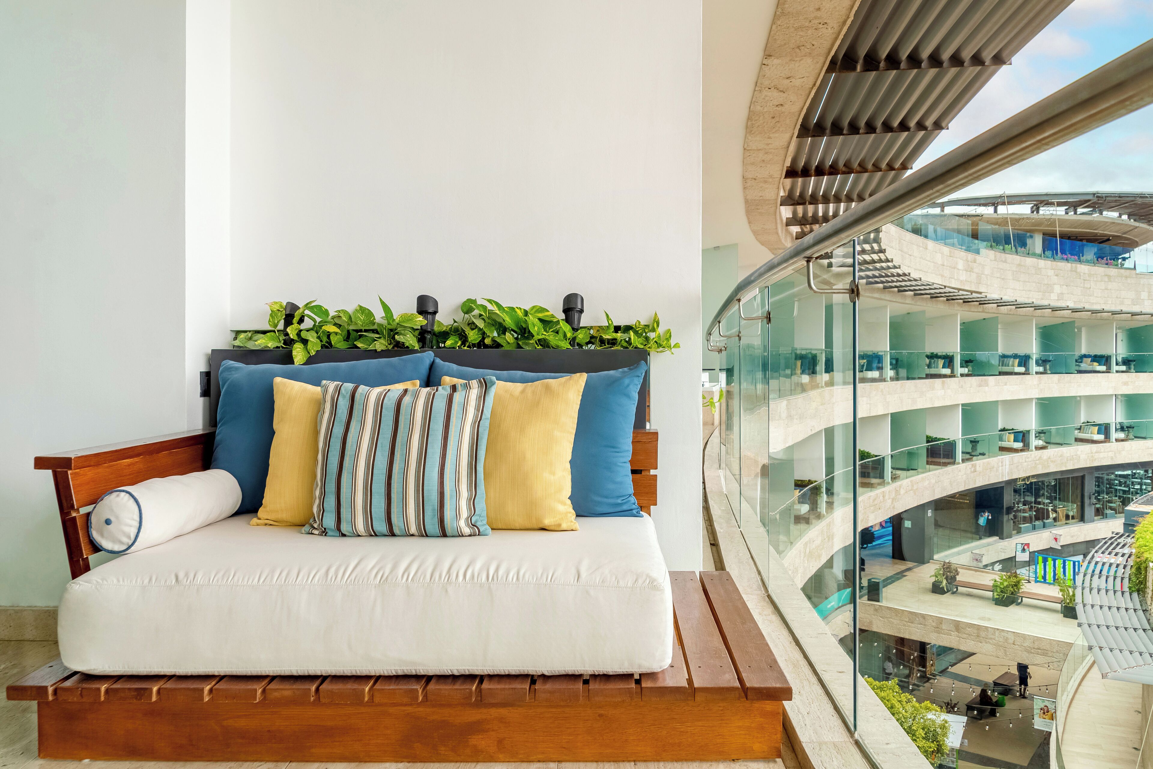 A modern hotel room with a wooden bench, a white sofa, and a view of the building's interior.