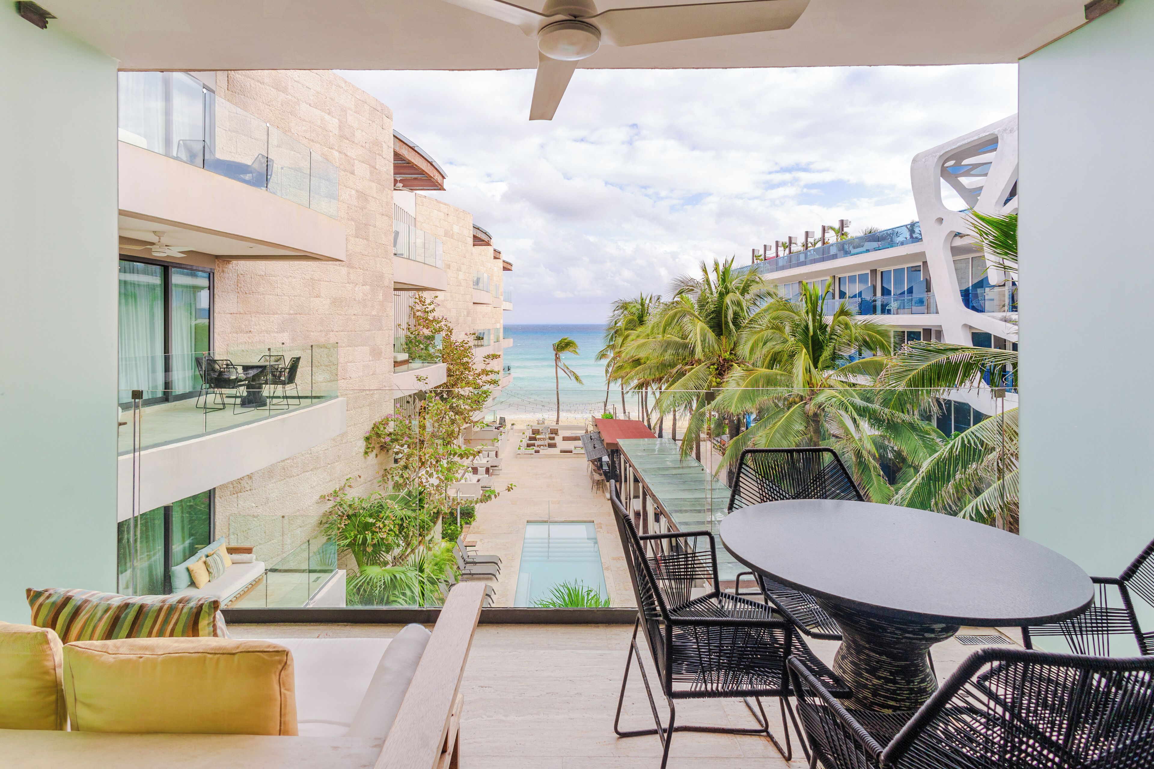 A balcony with a view of the ocean, a pool, and a dining area with chairs and a table.