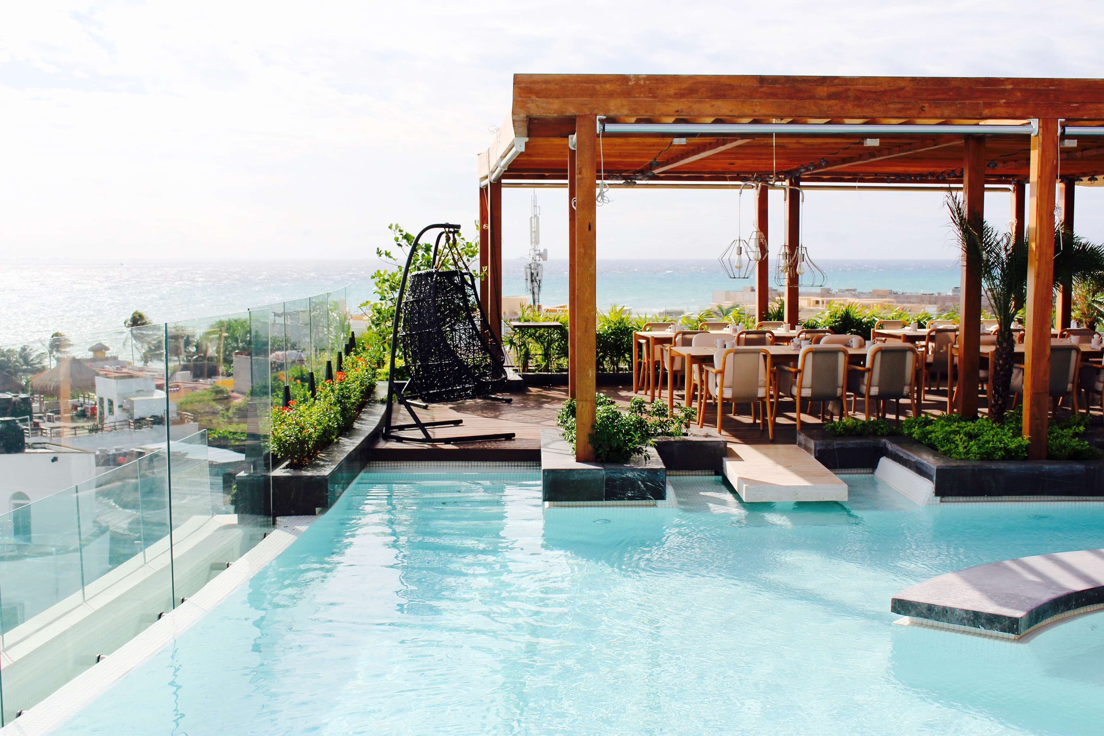 Una piscina en la azotea con una pérgola de madera, zona de estar y vistas al océano.