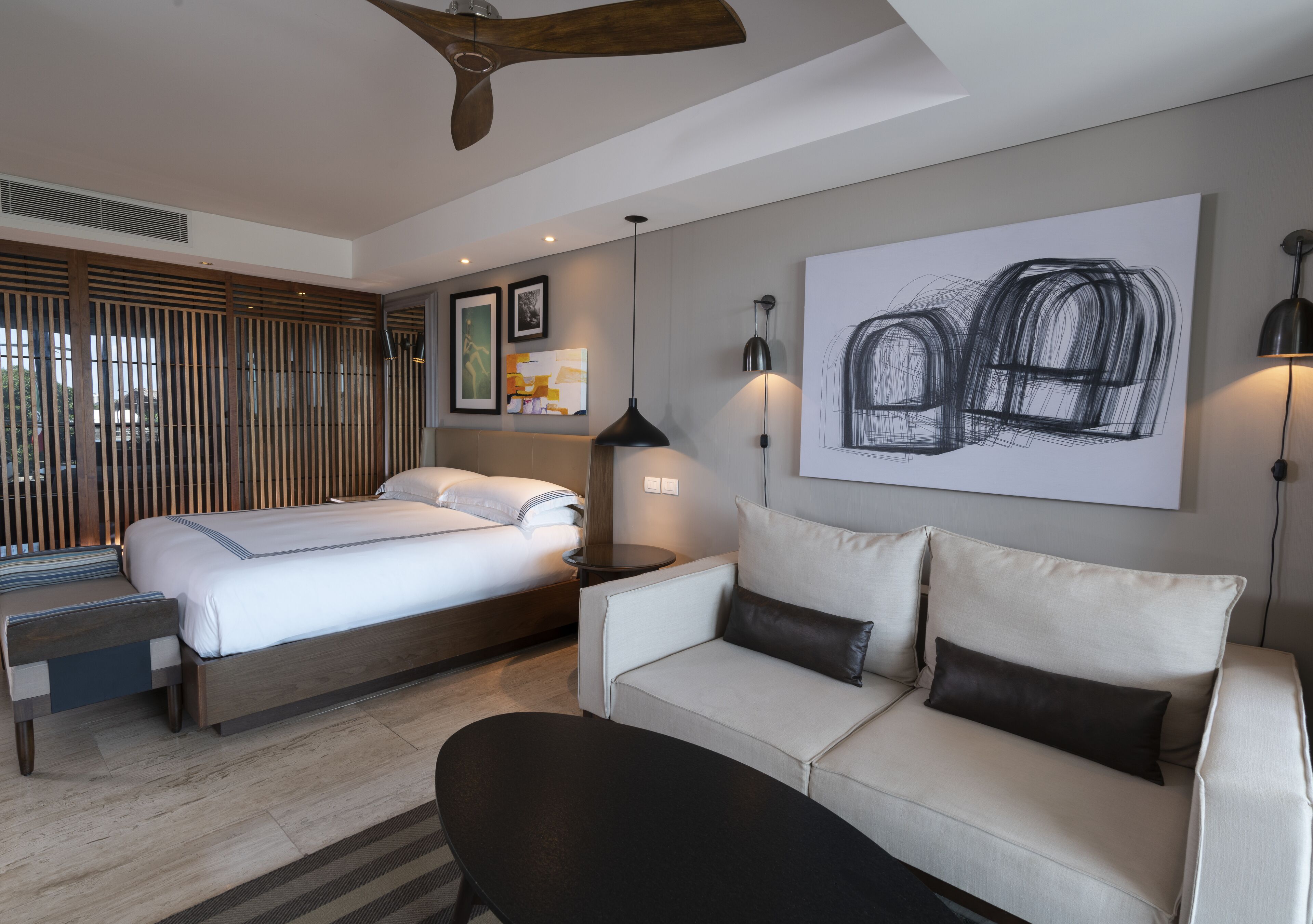 Una habitación de hotel moderna con cama, sofá, escritorio y un cuadro abstracto grande en la pared.