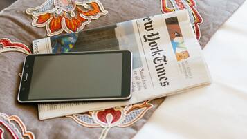 A bed with a floral-patterned bedspread, a tablet, and a folded newspaper.