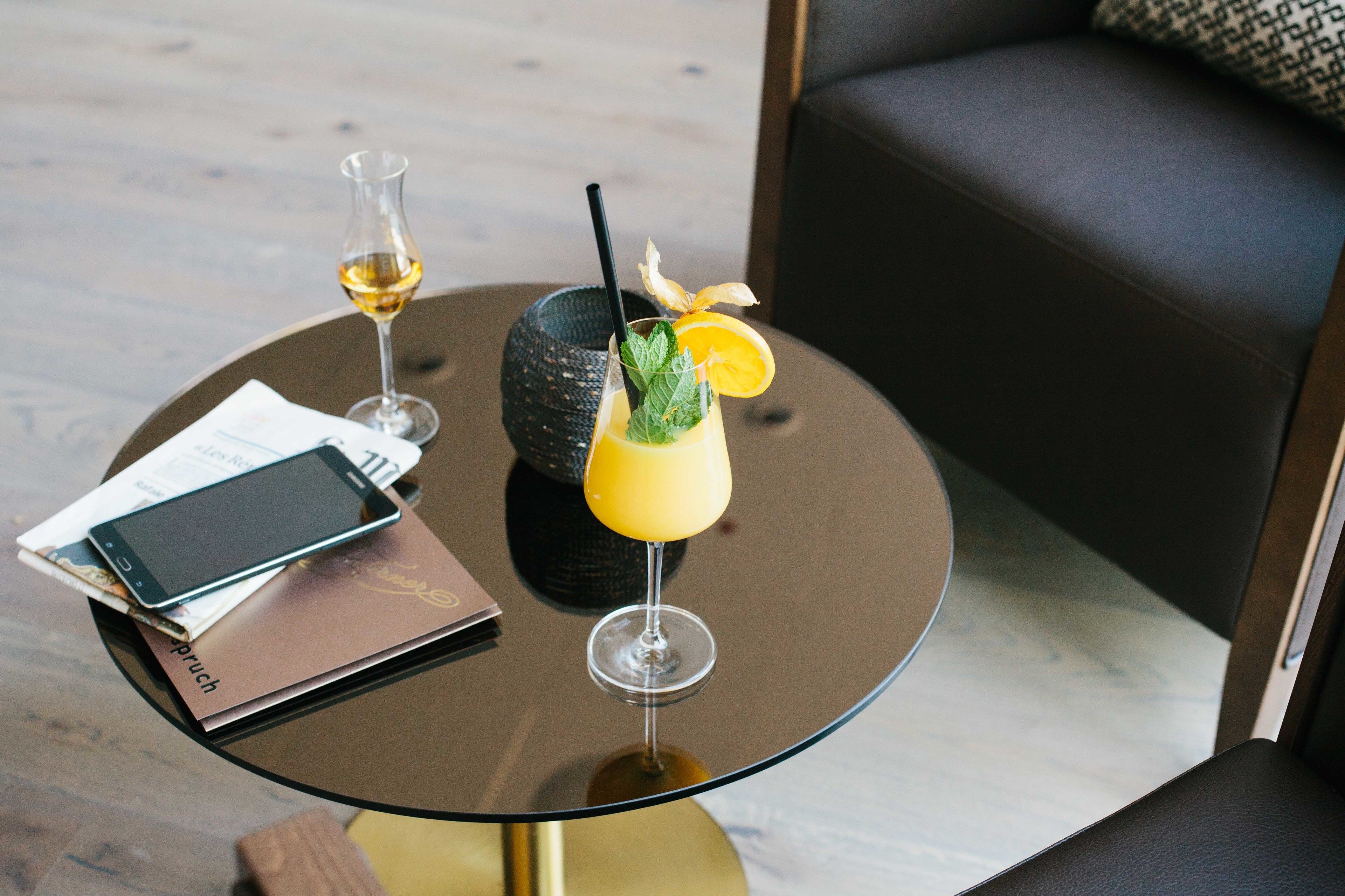 A glass table with a smartphone, a menu, and a cocktail with a straw and garnish.