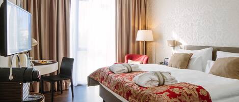 A hotel room with a bed, a desk with a chair, a television, and a window with curtains.