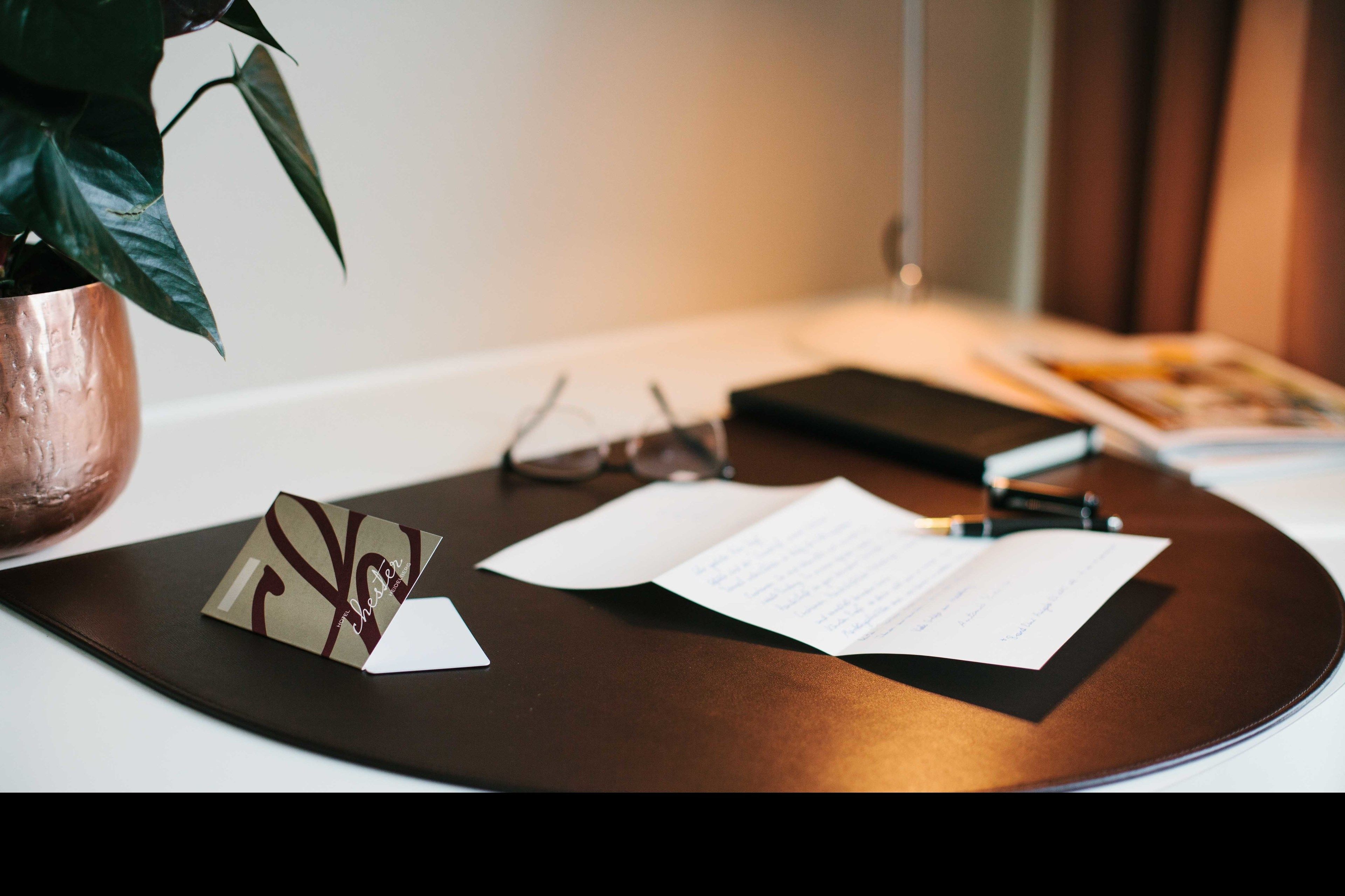 A desk with a notebook, glasses, a pen, and a plant.