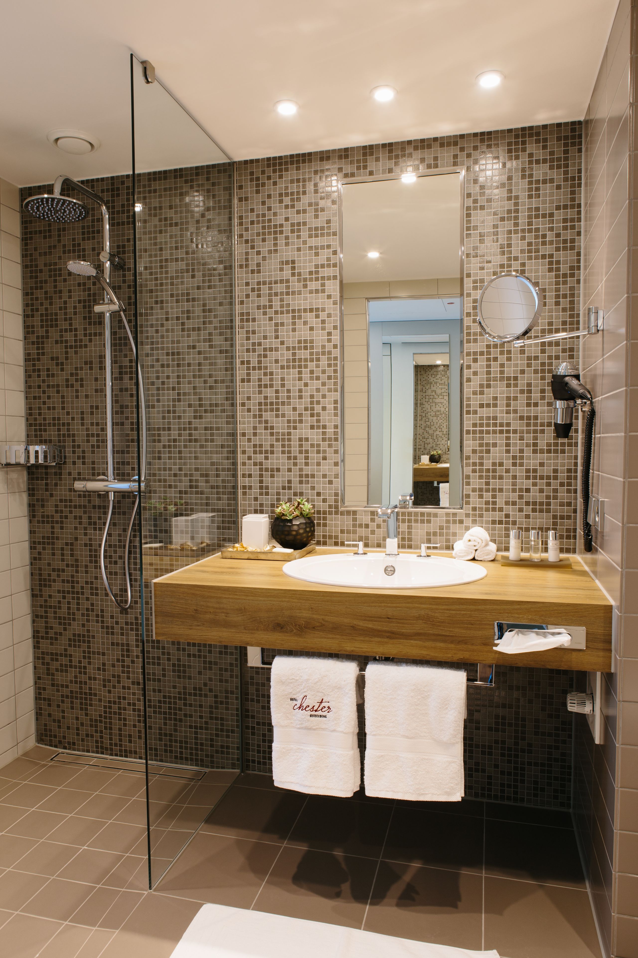 Ein modernes Badezimmer mit einem Holzlagerfläschchen, einem großen Spiegel, einer Duschkabine aus Glas und einer gefliesten Rückwand.