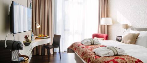 A hotel room with a bed, a desk with a coffee machine, a chair, a TV, and a window with curtains.