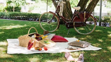 A picnic setup with a wicker basket, food, and a bicycle on a blanket.
