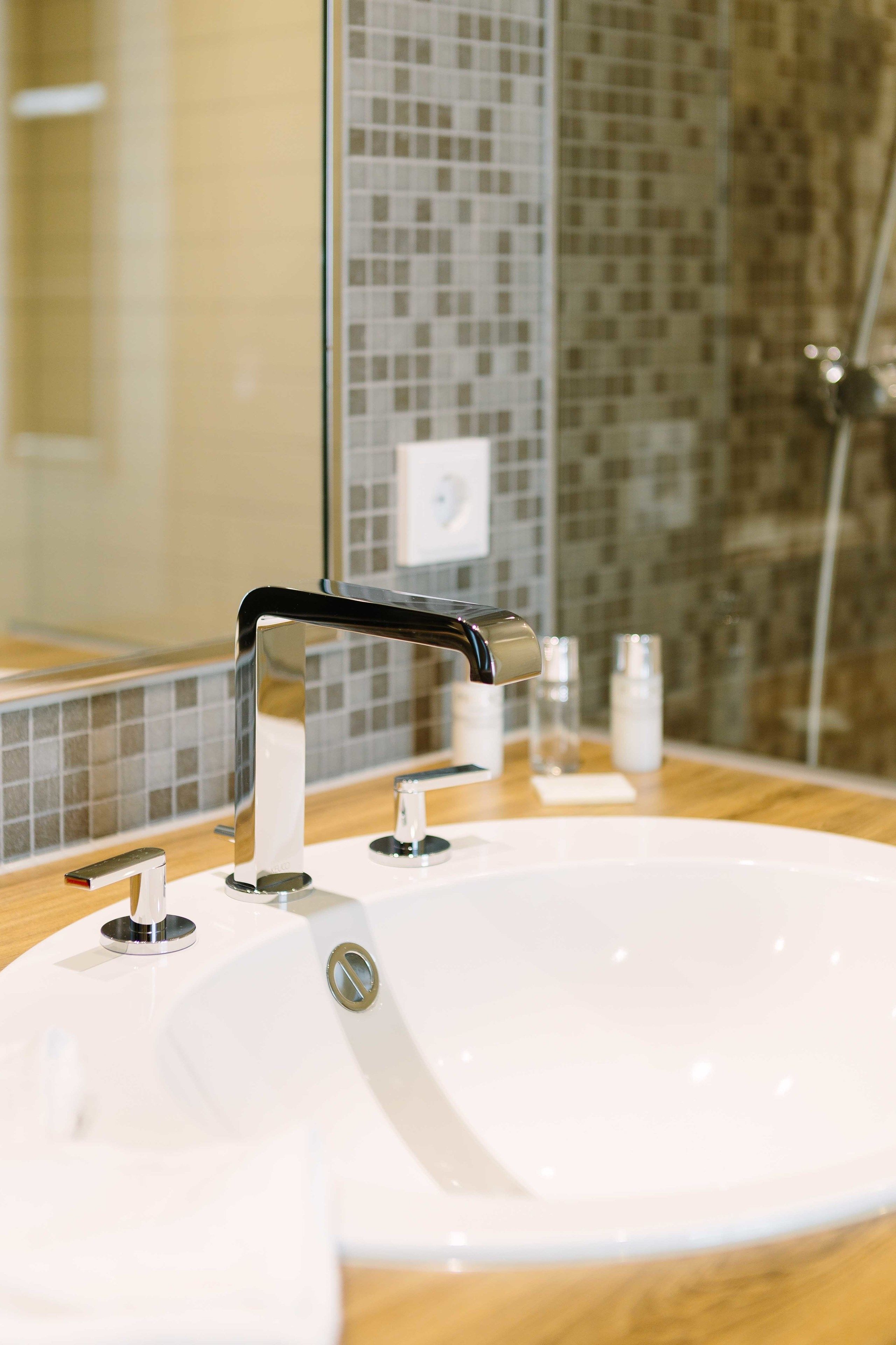 A bathroom with a white sink, chrome faucet, and a mirror reflecting a tiled backsplash.