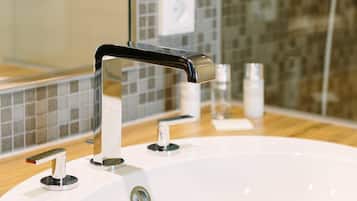 Un baño con lavamanos blanco, grifo cromado y un espejo que refleja un salpicadero azulejado.