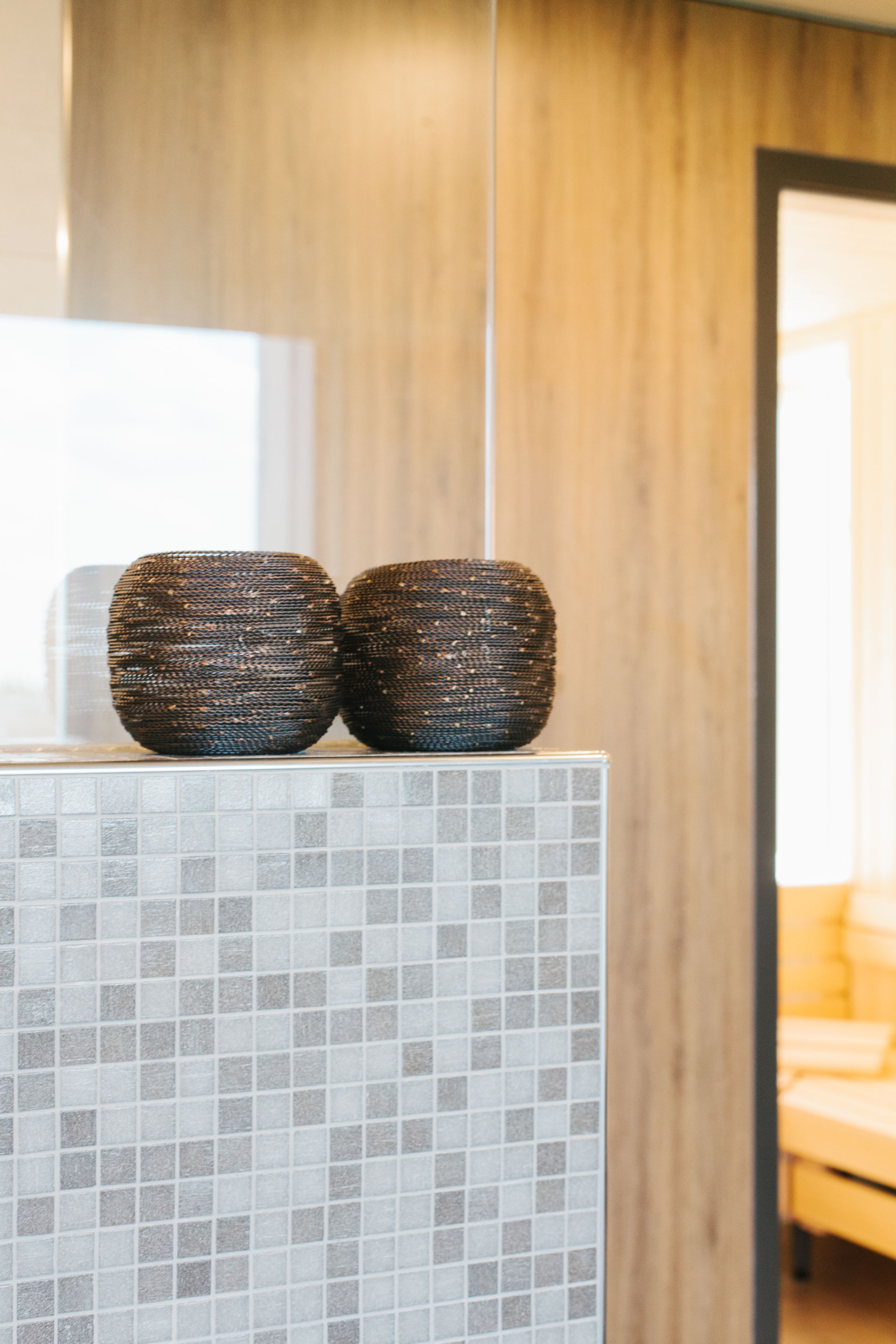 A bathroom with a tiled wall, two woven baskets on a counter, and a wooden panel in the background.