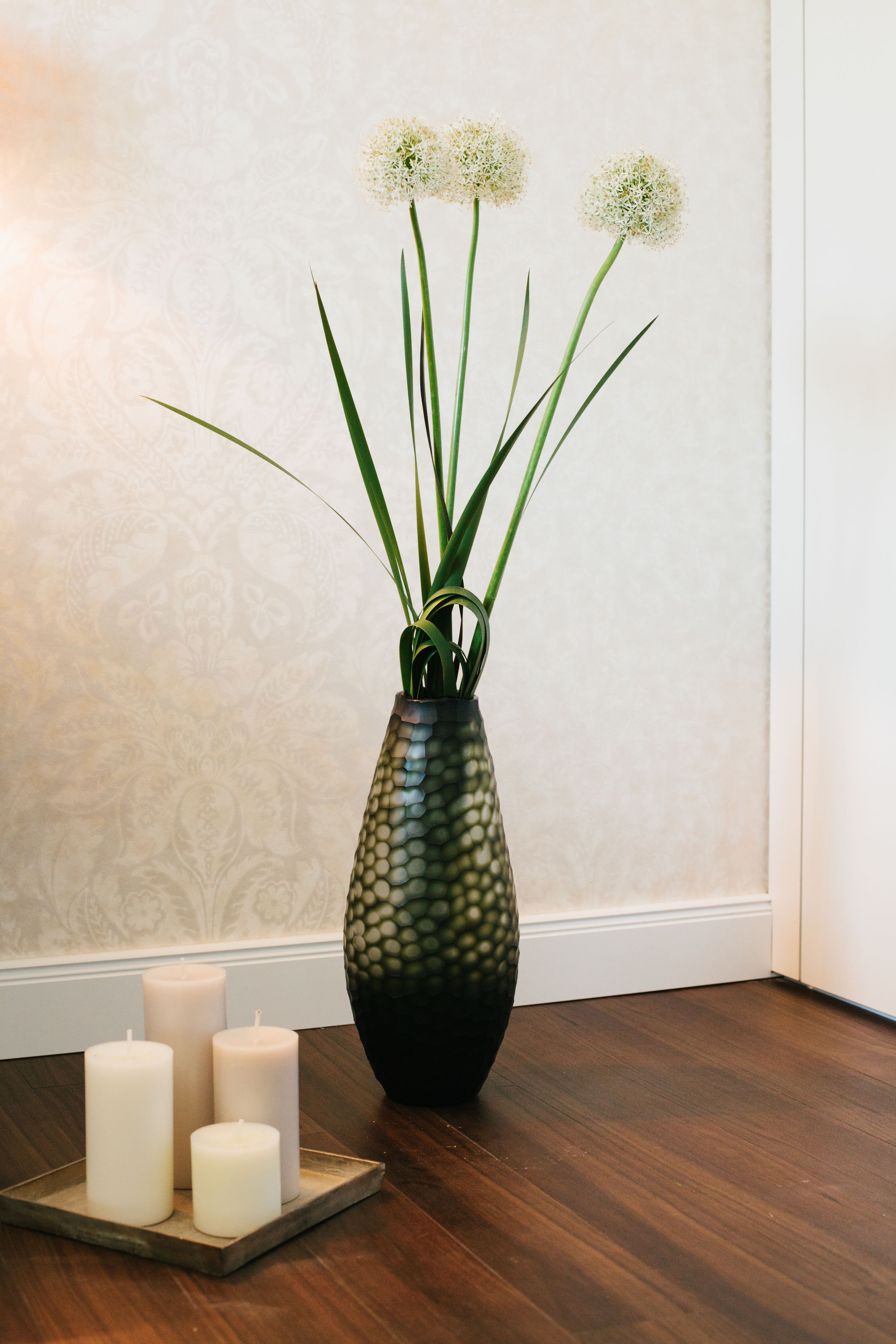 A vase with a textured pattern and three candles on a wooden tray.