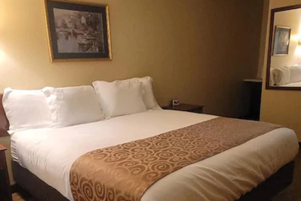 A hotel room with a large bed, a nightstand, a framed picture on the wall, and a small table with a lamp.