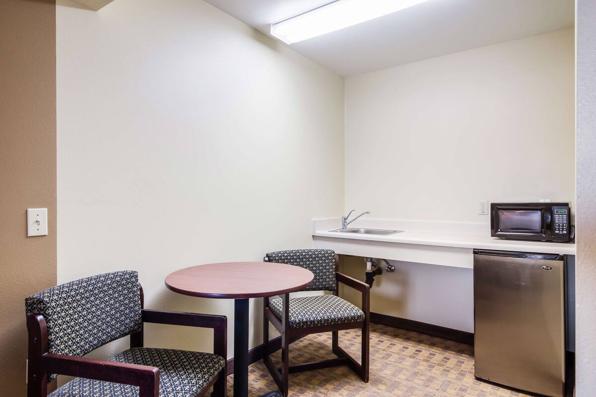 A compact kitchenette with a microwave, sink, and refrigerator. There are two patterned chairs and a small round table.