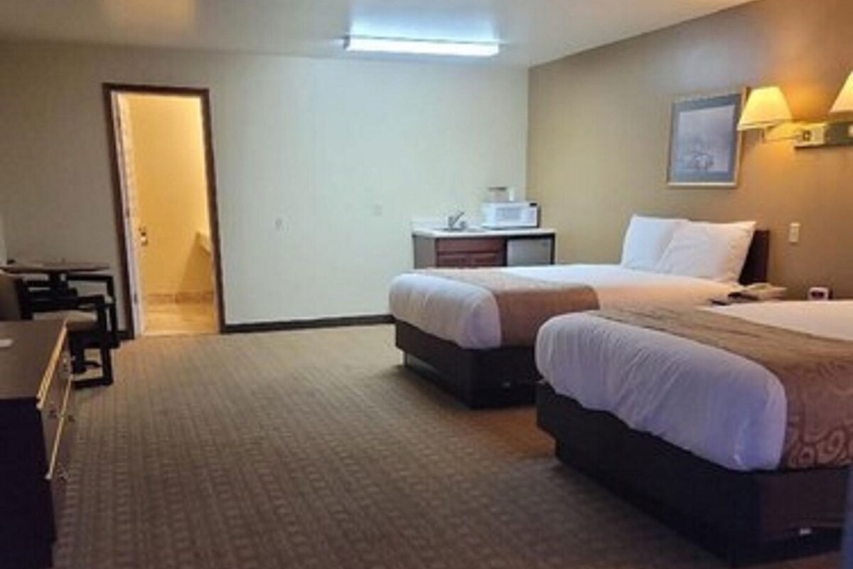 A hotel room with two beds, a desk, a chair, a nightstand, and a lamp.