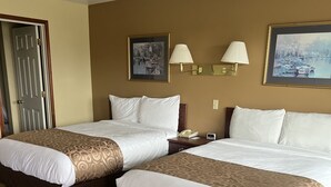 A hotel room with two beds, a door, a lamp, and two framed pictures on the wall.