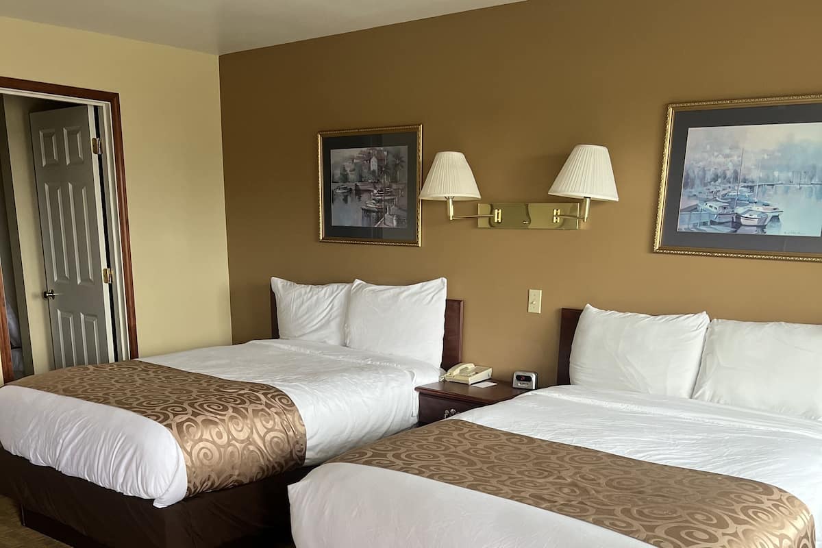 A hotel room with two beds, a door, a lamp, and two framed pictures on the wall.