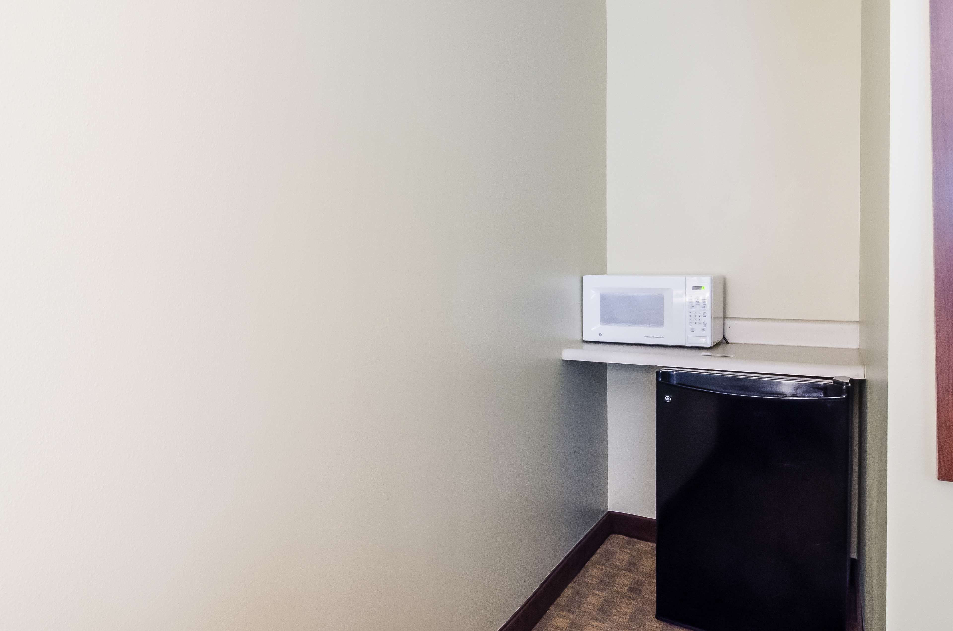 A compact kitchen with a microwave on a shelf and a black refrigerator.