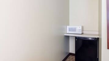 A compact kitchen with a microwave on a shelf and a black refrigerator.
