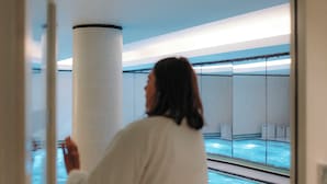 A person in a white robe standing in a room with a large window overlooking a pool. - Hôtel Eiffel Blomet (Paris)