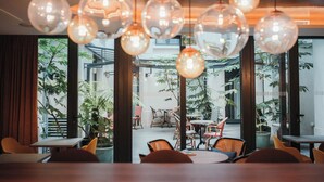 A modern interior with hanging spherical light fixtures, a view of an outdoor seating area with tables and chairs, and large windows allowing natural light. - Hôtel Eiffel Blomet (Paris)