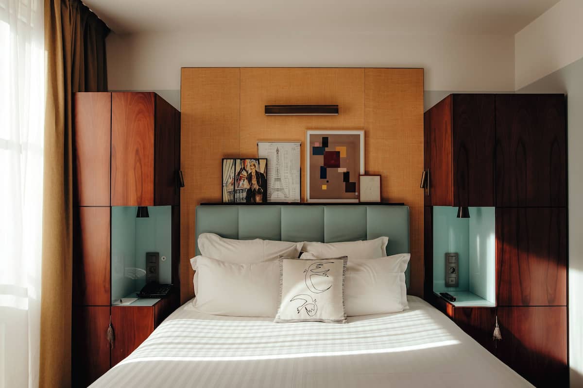 A neatly arranged hotel room with a large bed, wooden headboard, and a small bedside table with a lamp.