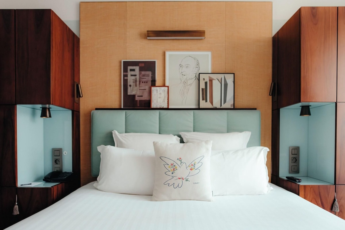 A modern hotel room with a large bed, a wooden headboard, and artwork on the wall.