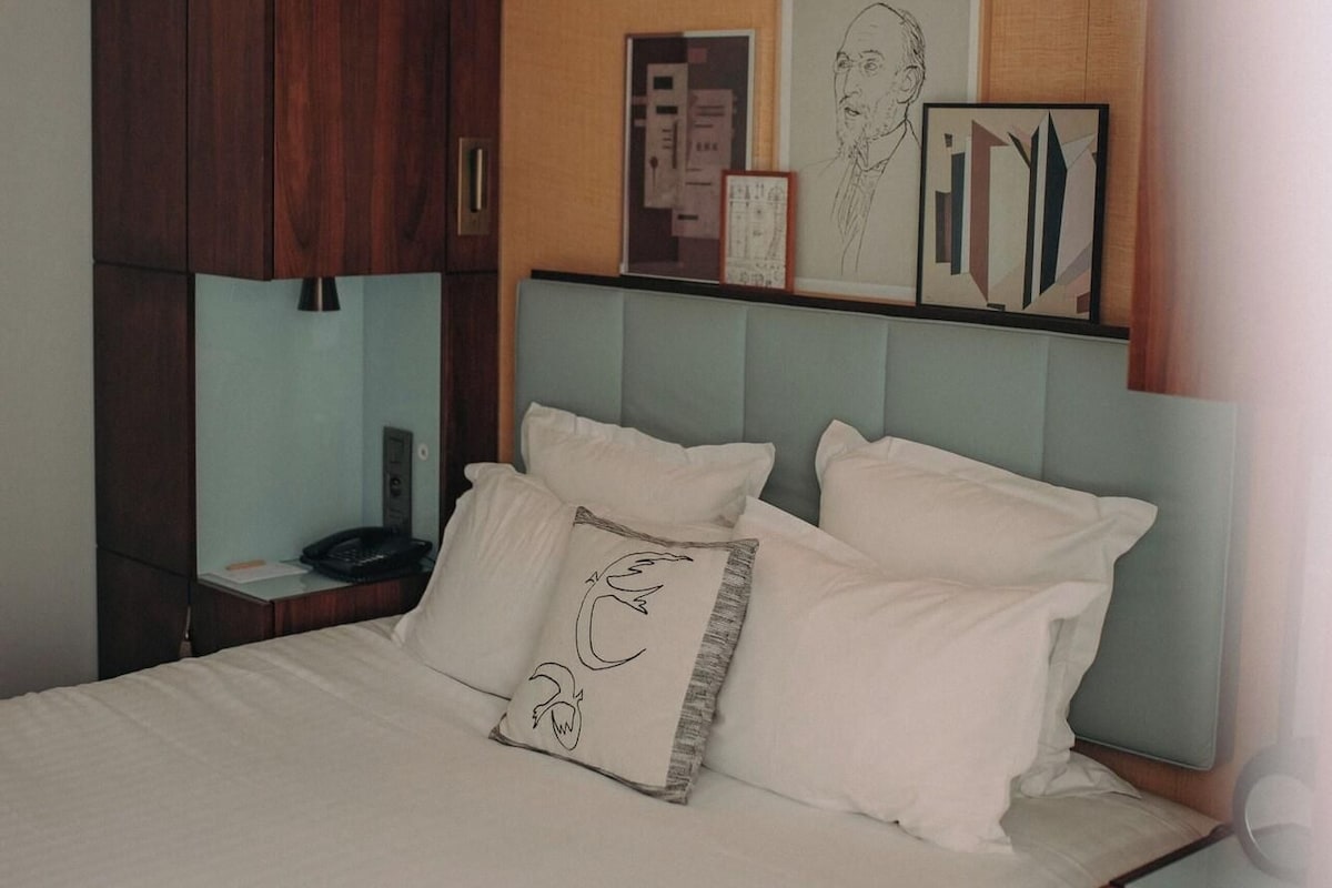 A neatly made bed with white linens and decorative pillows, a wooden headboard, and a bedside table with a lamp.
