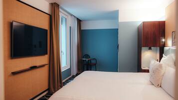 A hotel room with a large bed, a flat-screen TV mounted on the wall, a small table, and a chair.