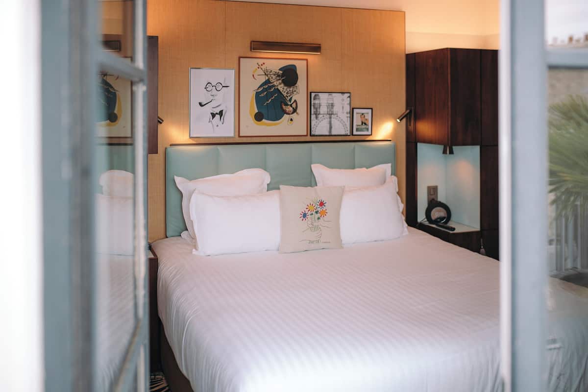 A neatly made bed with a light blue headboard, white bedding, and a decorative pillow. There are framed artworks on the wall above the bed.