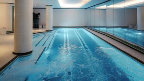 A modern indoor swimming pool with clear water, surrounded by tiled walls and columns, and a bright ceiling. - Hôtel Eiffel Blomet (Paris)