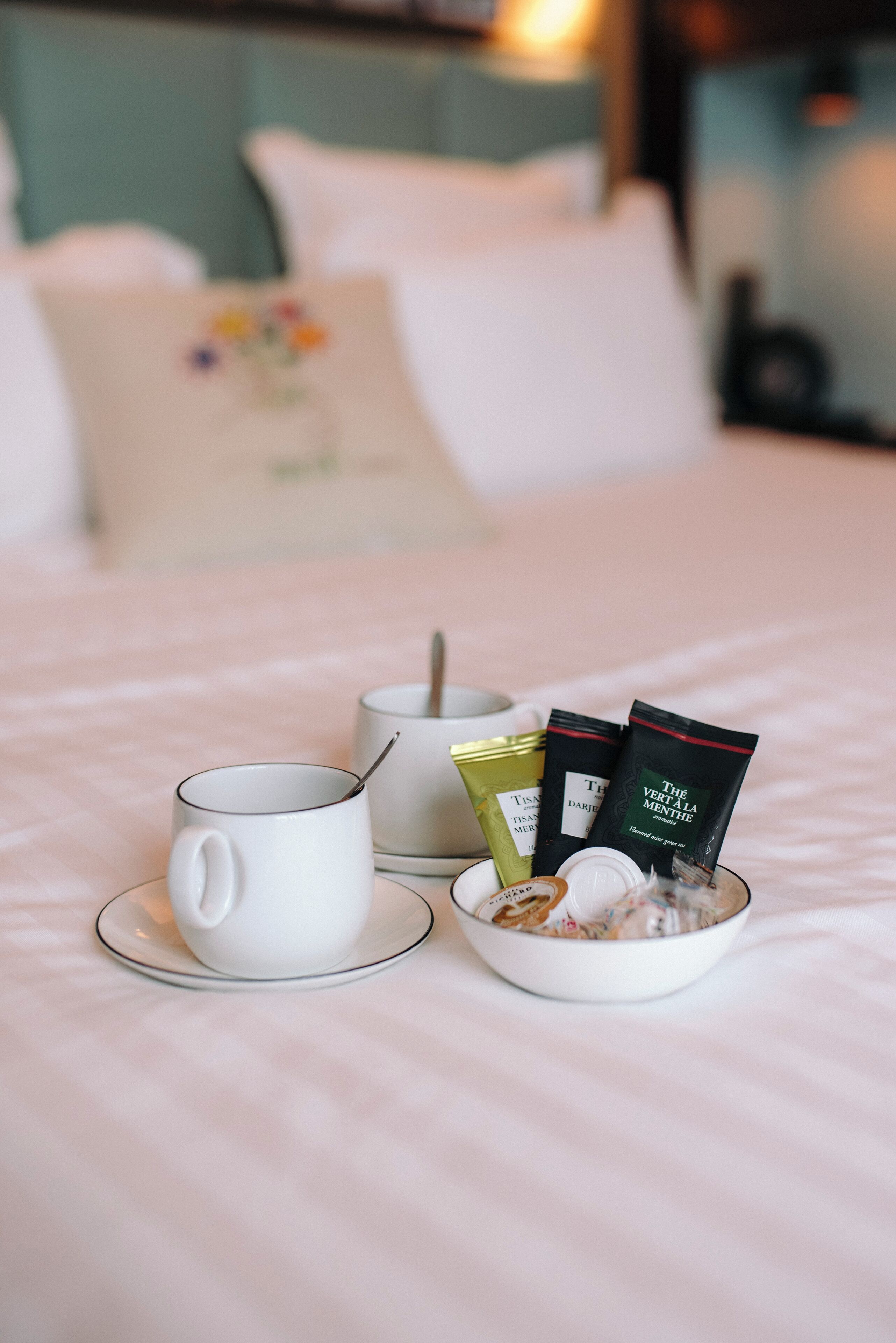 Een keurig opgemaakt ontbijt op een bed, bestaande uit een witte mok, een kom cornflakes en twee theezakjes op een witte tafelkleed.