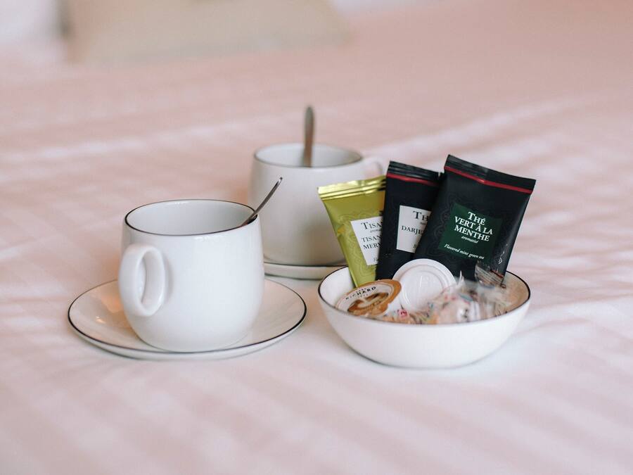 Een keurig opgemaakt ontbijt op een bed, bestaande uit een witte mok, een kom cornflakes en twee theezakjes op een witte tafelkleed.