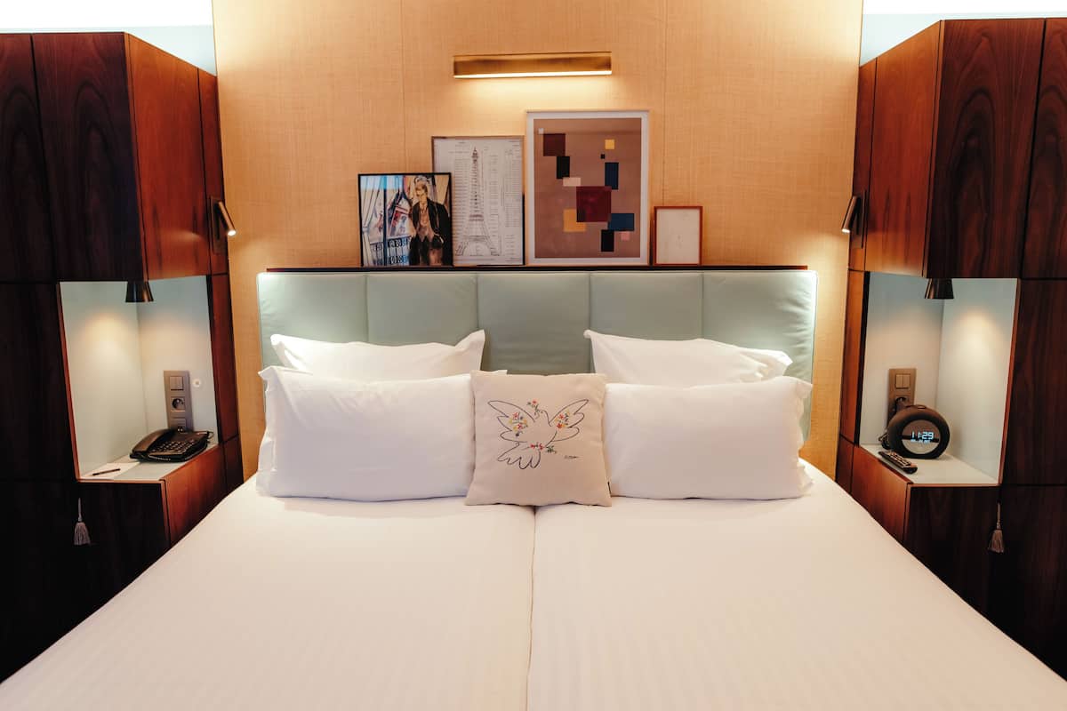 A hotel room with a large bed, two bedside tables, a nightstand, a wall-mounted clock, and framed artwork.