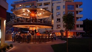 A circular outdoor bar area with multiple seating arrangements, surrounded by a multi-story building with balconies and a swimming pool. - Hotela Panorama Vigo (Nessebar)