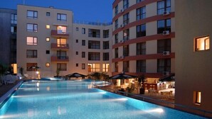 A swimming pool surrounded by a multi-story hotel with balconies and outdoor seating. - Hotela Panorama Vigo (Nessebar)