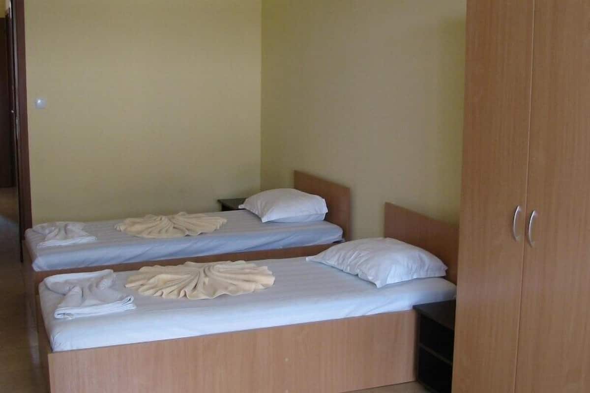 Zwei Einzelbetten mit Holzrahmen und weißer Bettwäsche, ein Holzschrank und eine schlichte Wand.