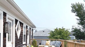 A wooden deck with outdoor furniture, including chairs and a sofa, and a view of a building in the background. - Salt House Inn (Provincetown)