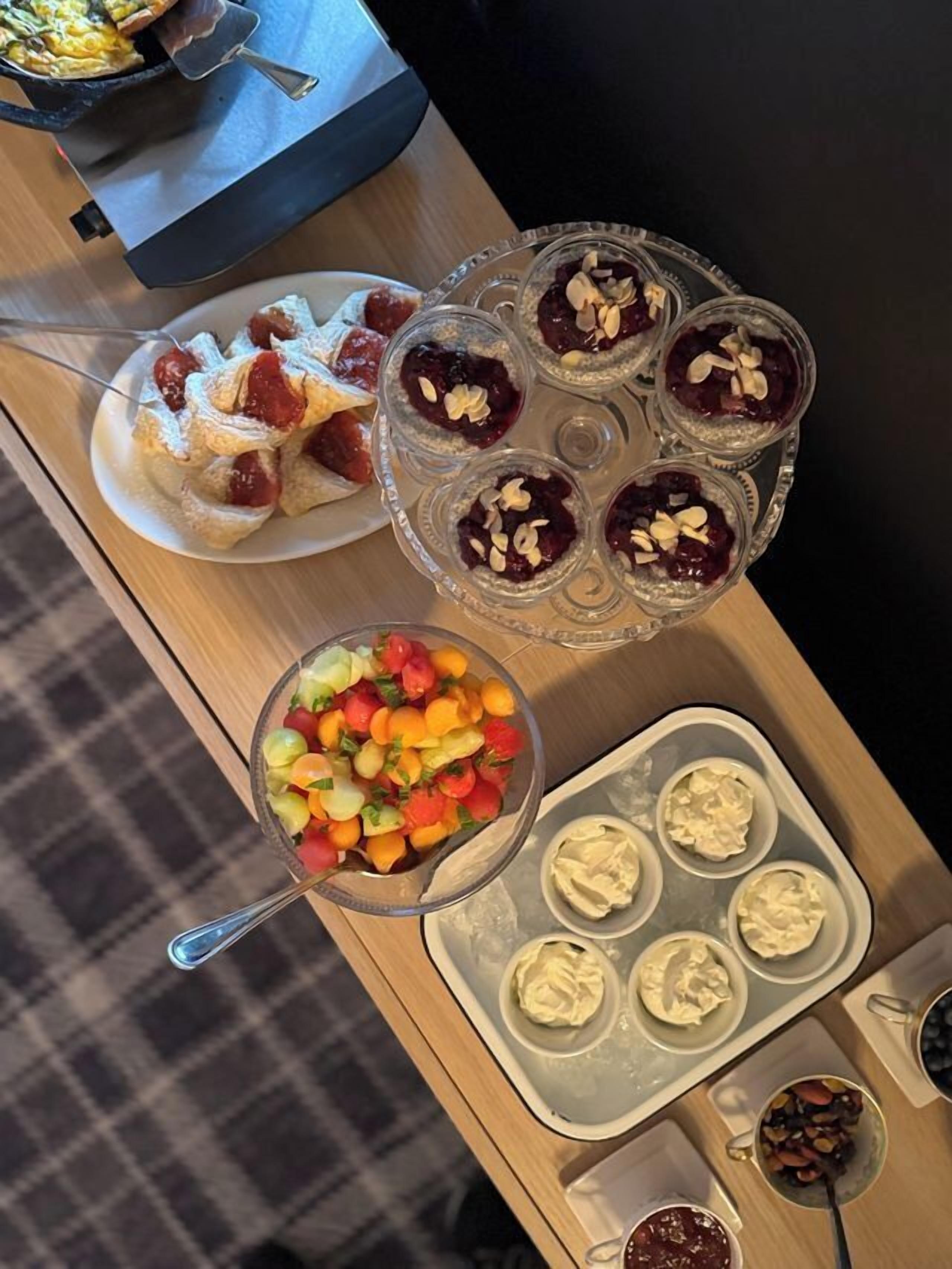 Uma mesa com diversos alimentos, incluindo salada de frutas, pastéis e sobremesas.