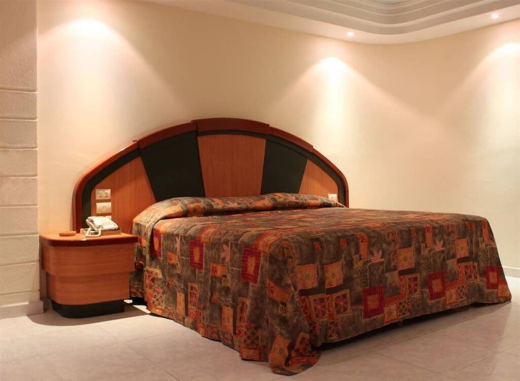 A bedroom with a wooden headboard, a bedside table with a lamp, and a patterned bedspread.