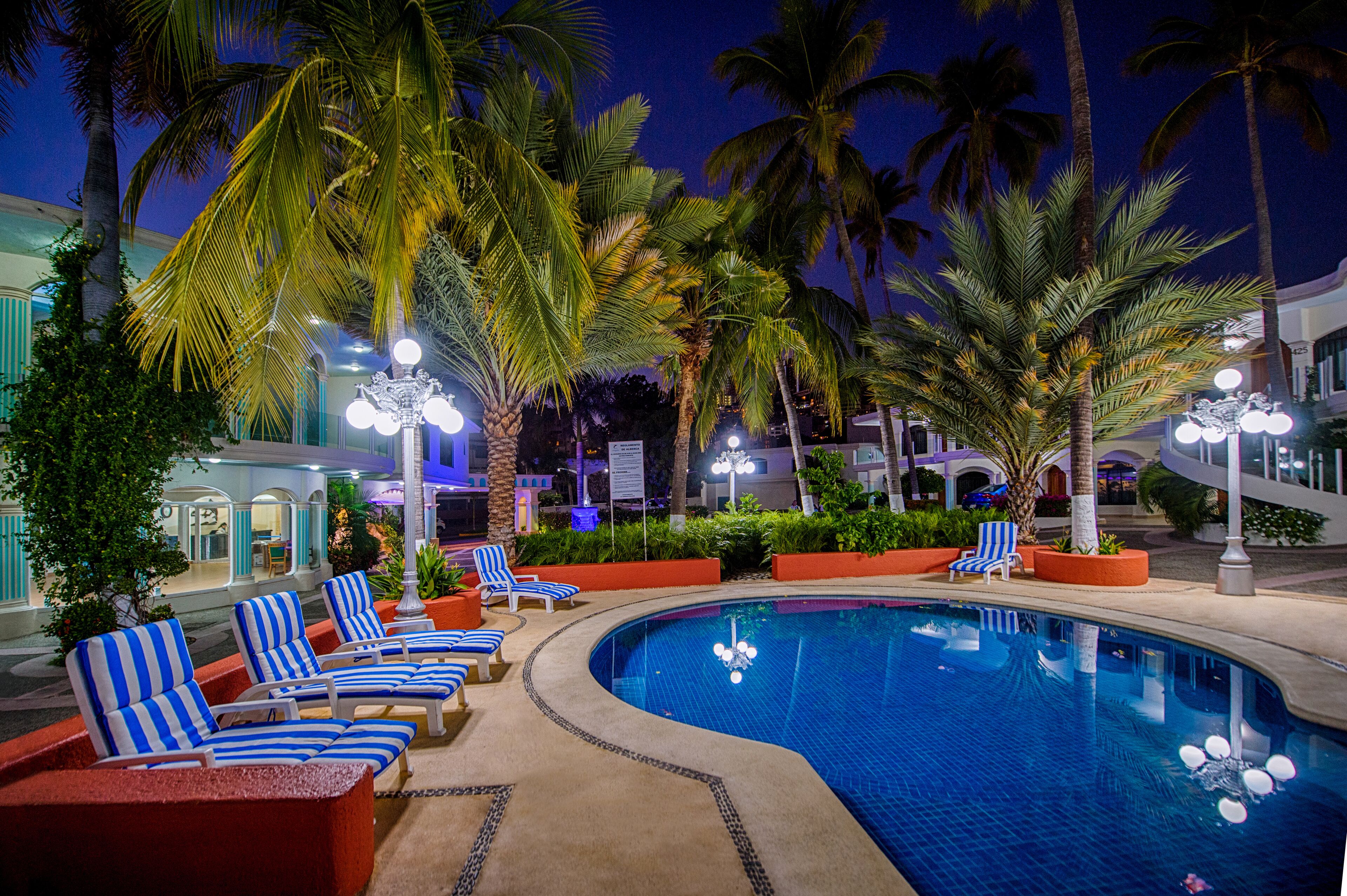 A pool area with lounge chairs and palm trees.