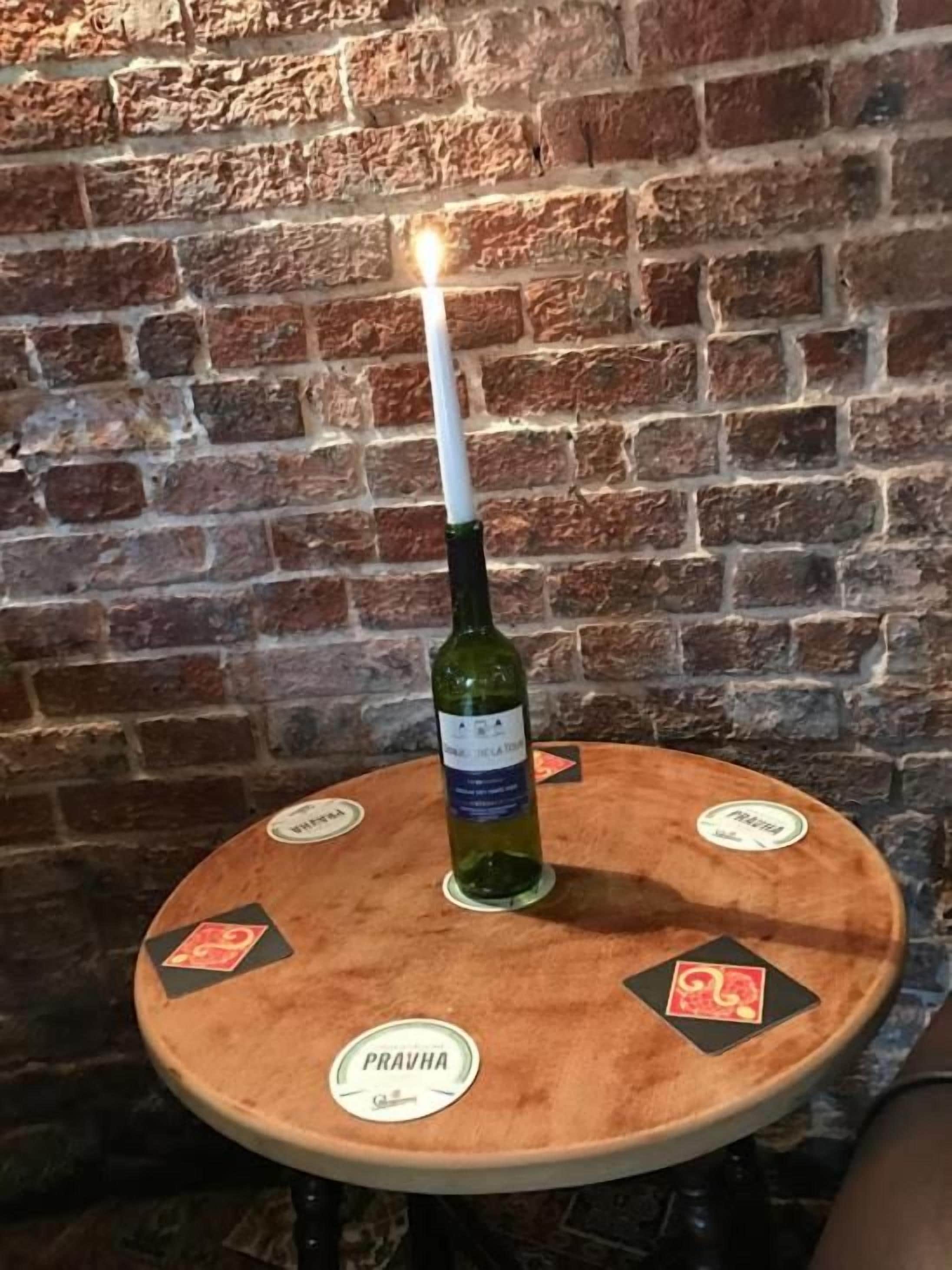 Une table ronde en bois, agrémentée d’une bougie allumée et d’une bouteille de vin, placée devant un mur de briques.