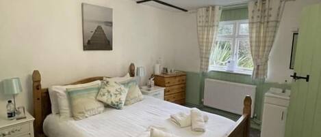 A bedroom with a wooden bed, bedside tables, a nightstand, a window with curtains, and a radiator.