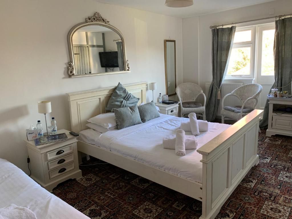 A hotel room with a large bed, a nightstand, a chair, a mirror, and a window with curtains.