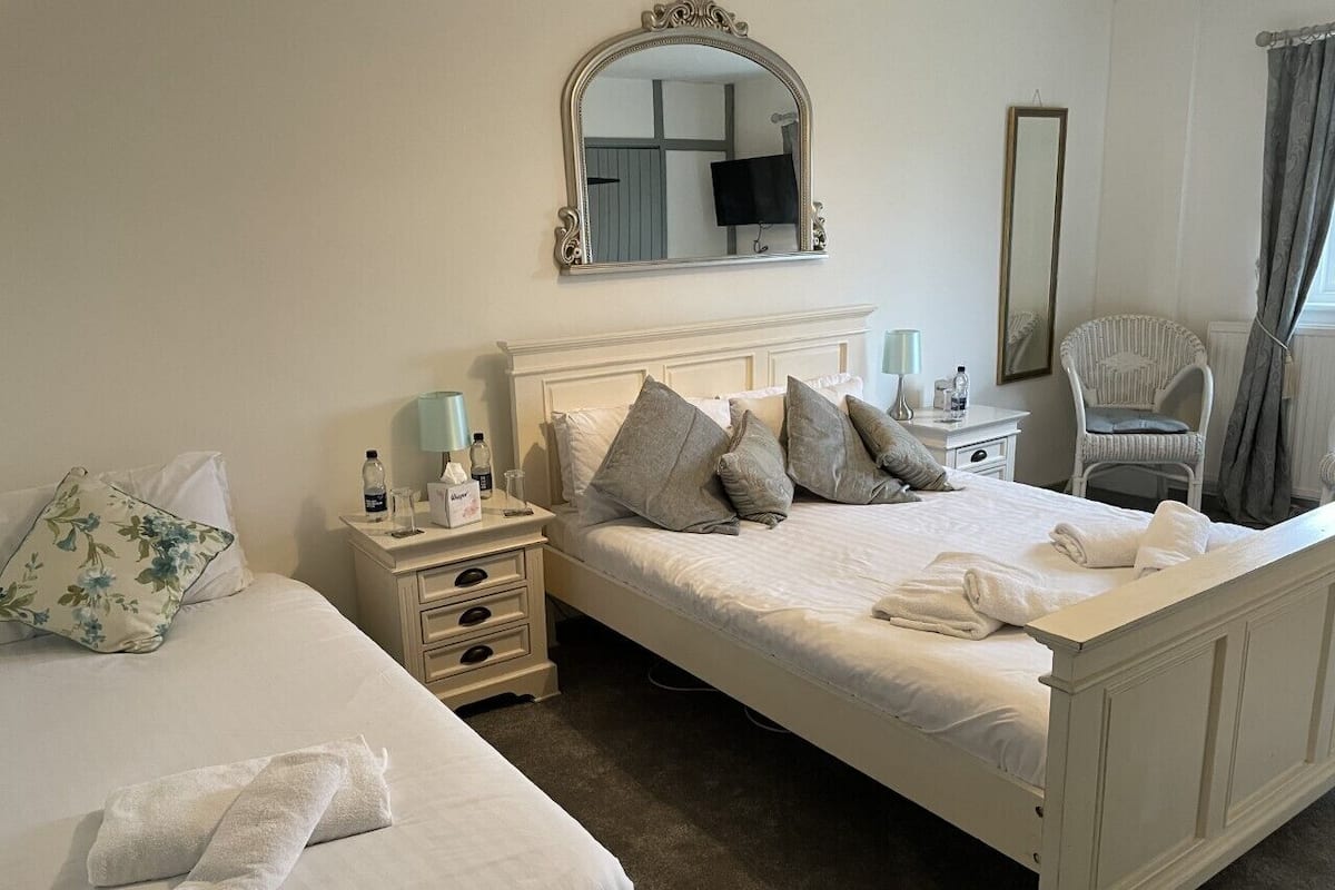 Une chambre d’hôtel avec un grand lit, un lit plus petit, une table de chevet avec des articles de toilette, un miroir et une chaise.
