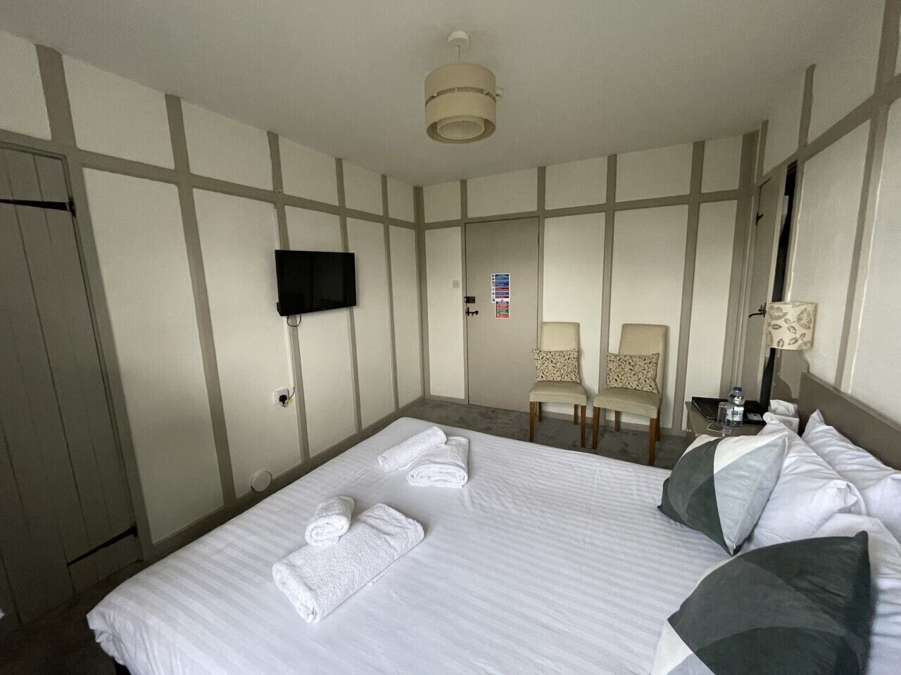 Habitación de hotel con una cama grande, dos sillas, un televisor y un escritorio con lámpara.