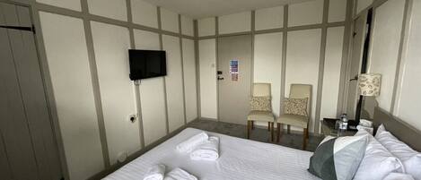 Habitación de hotel con una cama grande, dos sillas, un televisor y un escritorio con lámpara.