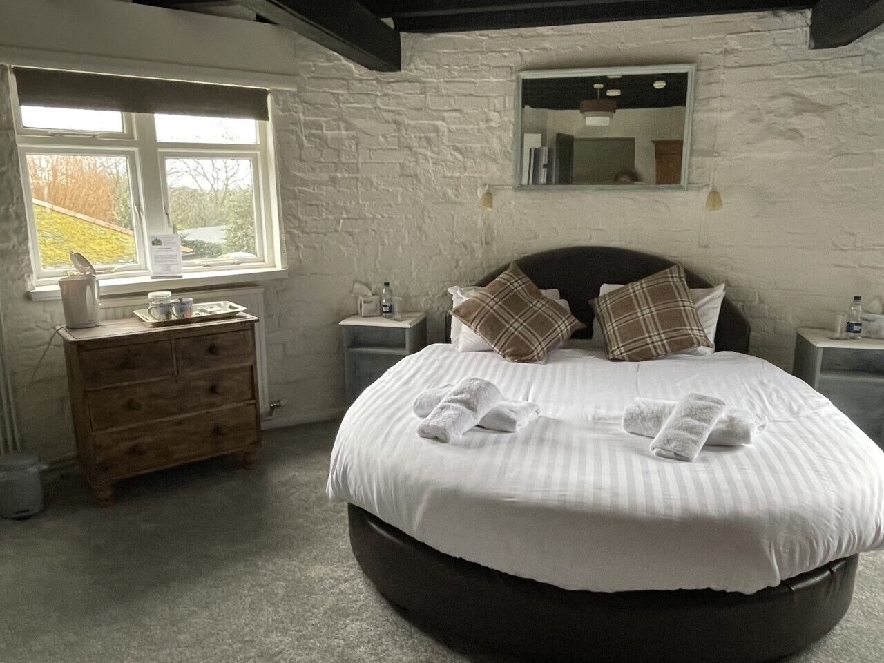 A bedroom with a large bed, a wooden dresser, a window, and a mirror on the wall.